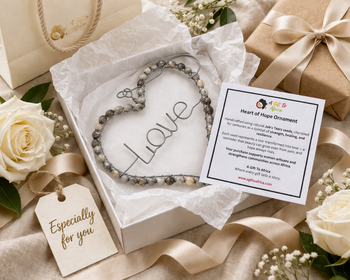 Heart-shaped 'Love' ornament with a tag and gift box on a decorative surface with flowers.